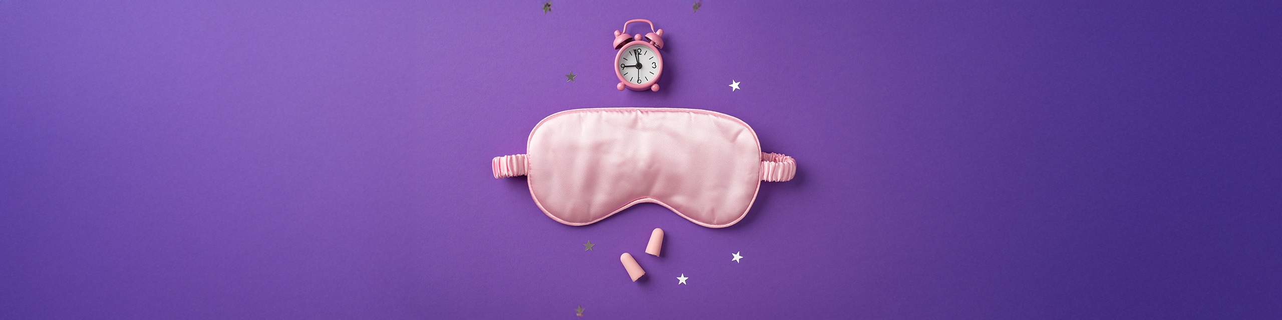 Pink sleep mask and nighttime essentials arranged on a purple surface, representing evening ritual essentials.