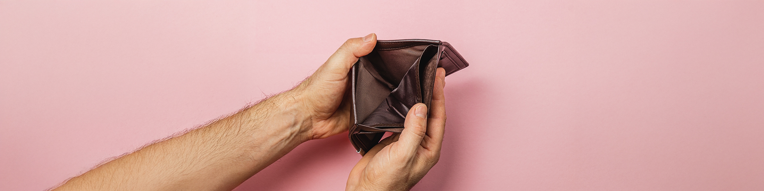 Close-up of hands opening an empty brown wallet on a pink background