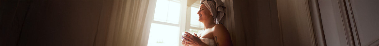 Woman standing by a window with morning light, holding a cup and enjoying a peaceful intentional morning ritual.