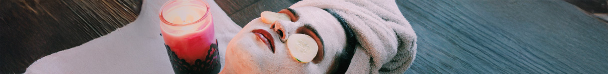 Woman relaxing with a facial mask, a towel wrap, and a lit candle, enjoying a soothing nighttime self-care moment.