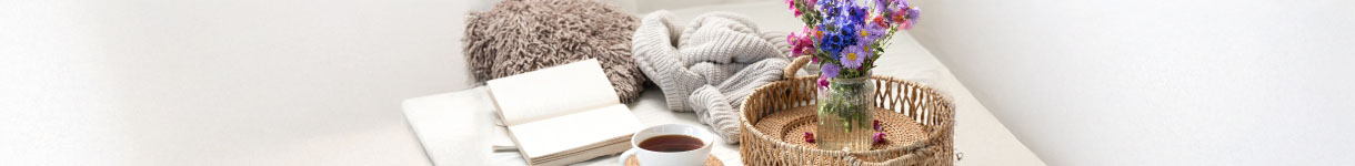 Bedside table with lavender flowers, a warm drink, notebooks, and soft blankets, illustrating a comforting lavender-inspired self-care space.