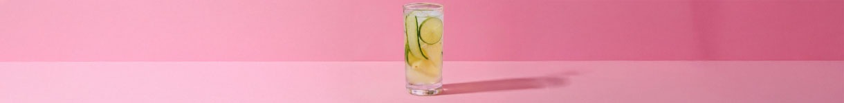 Minimalist cup of limonade with lemons slices on a pink background, illustrating the simplicity behind beauty product creation