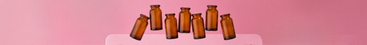 Amber glass bottles lined up on a pink surface, representing product formulation and fragrance testing in beauty brand development