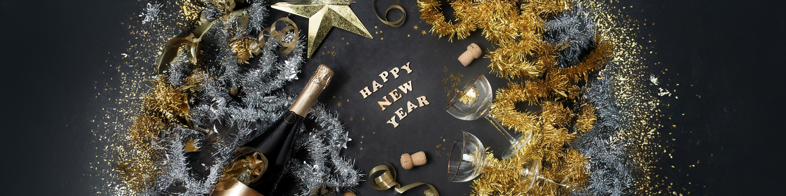Overhead view of champagne bottle, glitter, gold confetti, and party decorations for New Year’s celebration