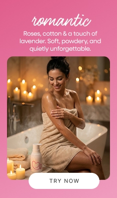 Woman in towel sitting on bathtub edge surrounded by candles applying Dear Me Romantic body lotion in a cozy luxury setting